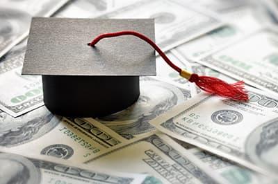paper graduation cap on top of pile of money